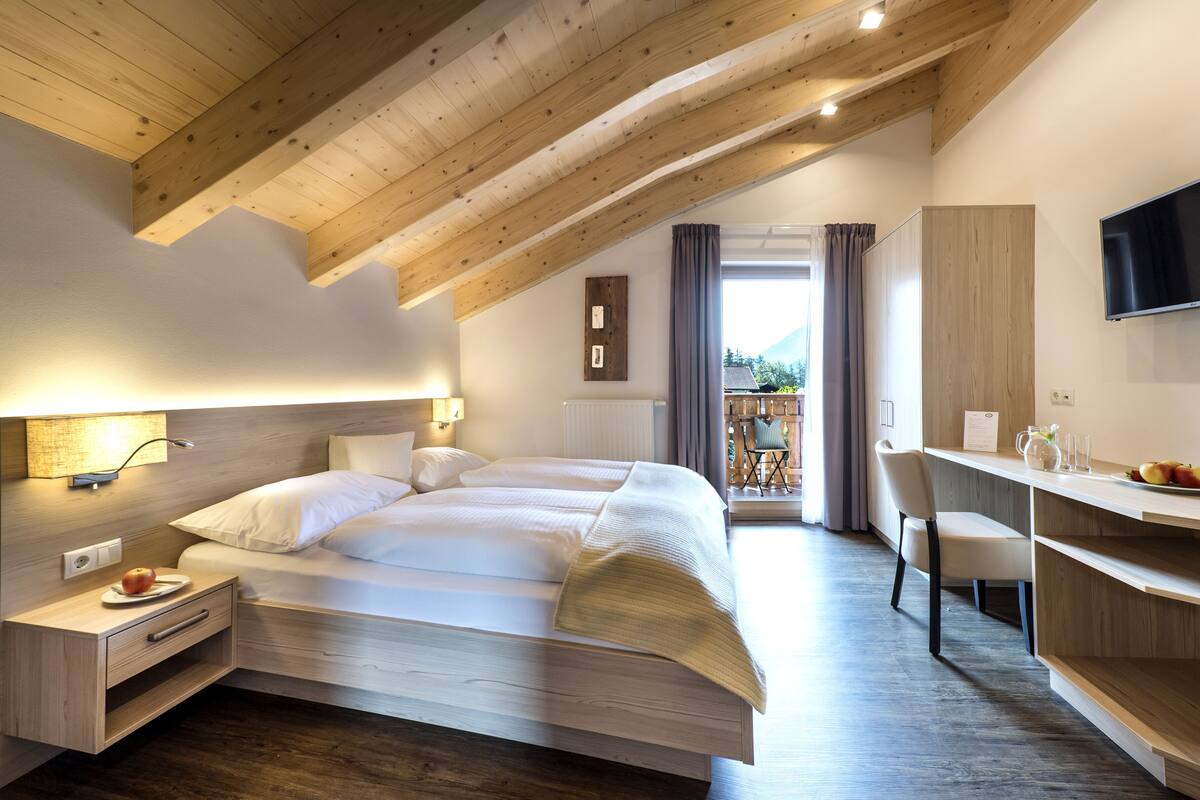 Un dormitorio moderno con techo estilo loft, cama, mesitas de noche, escritorio y vistas al exterior.