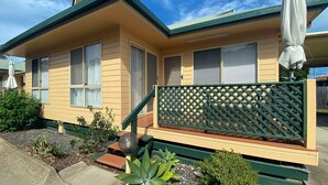 A two-story house with a green roof, beige siding, and a wooden deck with a lattice fence. - San Marco Villa 3 - Burrum Heads - Beachfront - 2BR - Pool (BURRUM HEADS)