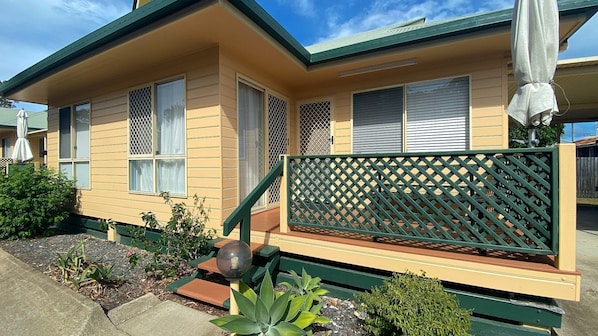 Une maison à deux étages avec un toit végétalisé, un revêtement extérieur de couleur beige et une terrasse en bois agrémentée d’une clôture à treillis.