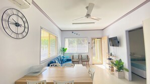 A dining area with a wooden table and chairs, a large wall clock, and a ceiling fan. - San Marco Villa 3 - Burrum Heads - Beachfront - 2BR - Pool (BURRUM HEADS)