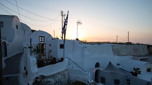 A coastal village with white-washed buildings, a prominent flag, and a sunset in the background. - Mylopetres (Santorini)