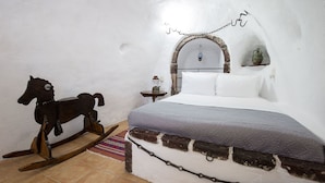 A bedroom with a bed, a wooden rocking horse, a small table with a lantern, and a wall-mounted shelf. - Mylopetres (Santorini)