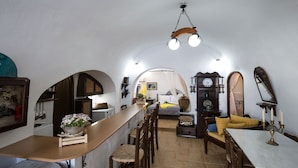 A cozy, well-lit room with a bed, a wooden table, and a dining area. - Mylopetres (Santorini)