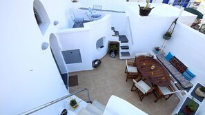 Eine Dachterrasse mit einem Holztisch, Stühlen und einer kleinen Sitzecke mit Kissen. Es gibt Kübelpflanzen und einen kleinen Tisch mit Stühlen.