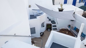 A white-walled building with a small patio area featuring a table, chairs, and a hanging shade. - Mylopetres (Santorini)