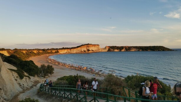 Una zona costera con playa, acantilados y una escalera que baja hacia la orilla.