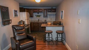 A compact kitchen with wooden cabinets, a refrigerator, a stove, and a sink. There are two stools at the kitchen island.