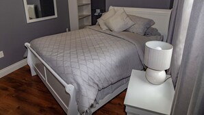 A bedroom with a bed, bedside tables, a mirror, and built-in shelving.