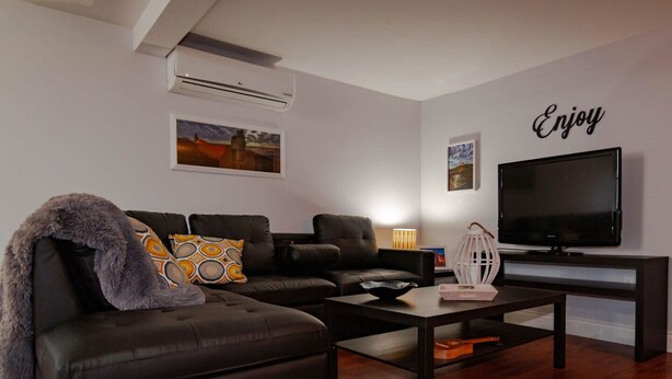 A modern living room with a black leather sofa, a coffee table, a flat-screen TV, and artwork on the walls.