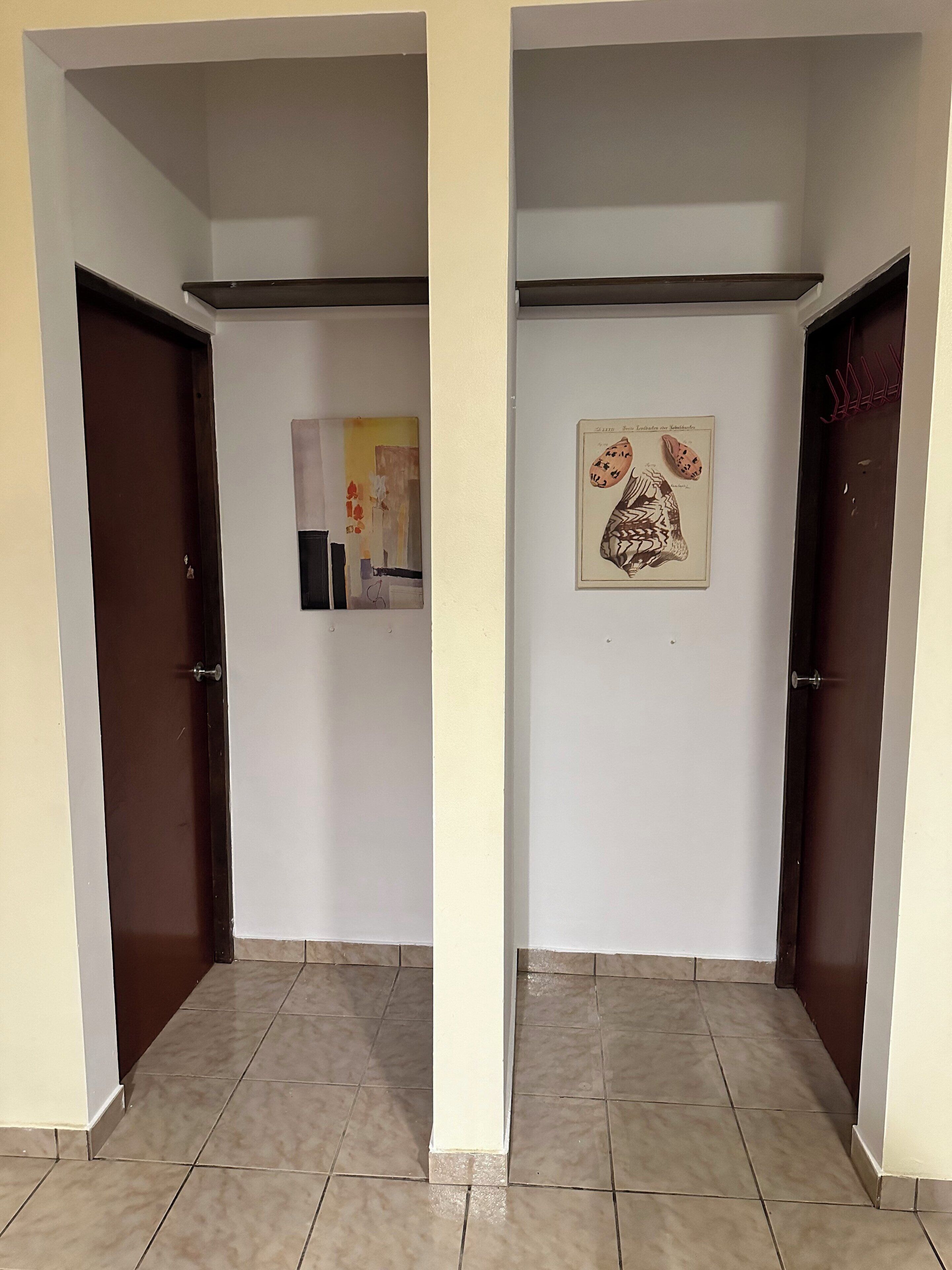 A hallway with two doors, a tiled floor, and two framed pictures on the walls.