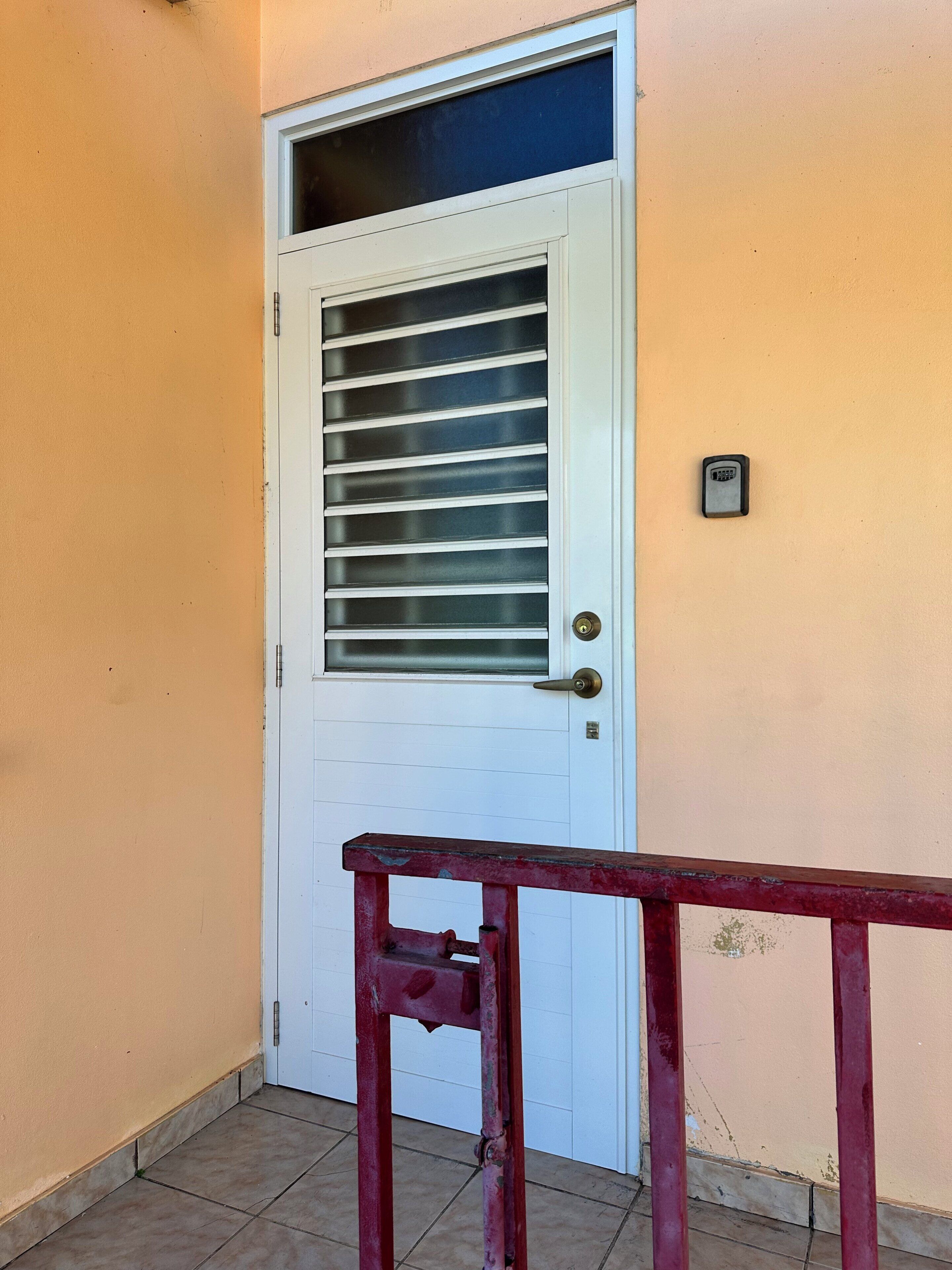 Une porte blanche, dotée d’une fenêtre et d’un clavier pour ouvrir à l’aide d’un code, se détachant sur un mur de couleur pêche.