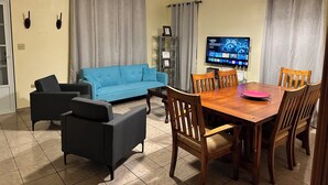 A living room with a blue sofa, a wooden dining table with chairs, a TV, and a ceiling fan. - A second story house at less than 5 min walking from beach (Aguada)