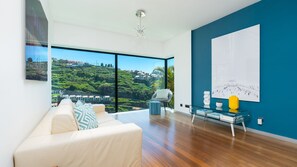 Un salon moderne doté d’une grande fenêtre, d’un canapé, d’une table basse en verre et offrant une vue sur une colline.