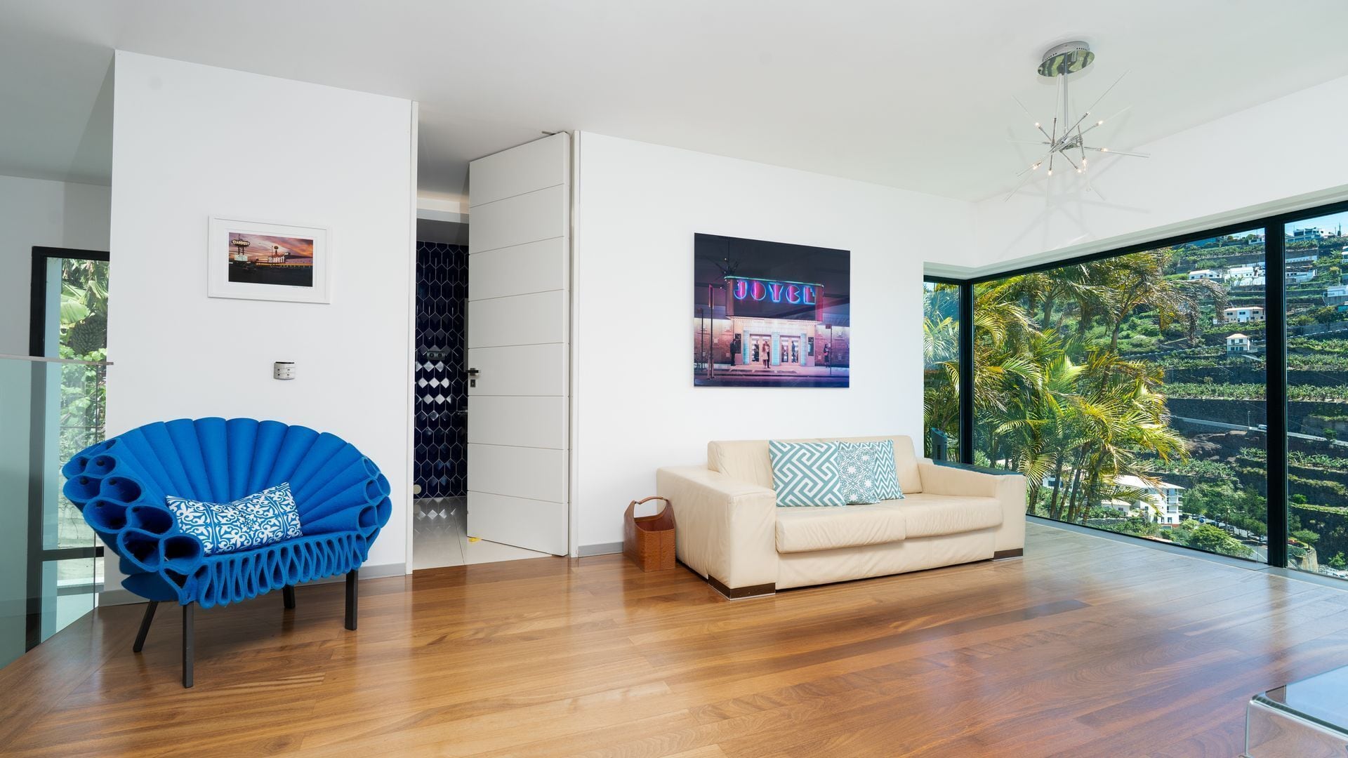 Een moderne woonkamer met een groot raam, een blauwe stoel, een beige bank en een lijst met een foto aan de muur.