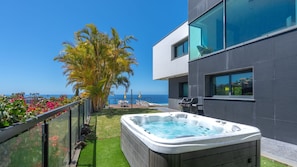 A modern building with a hot tub, a pool, and a view of the ocean.