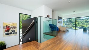 Un intérieur moderne avec un escalier, une cloison en verre, un canapé et une vue sur un paysage verdoyant.