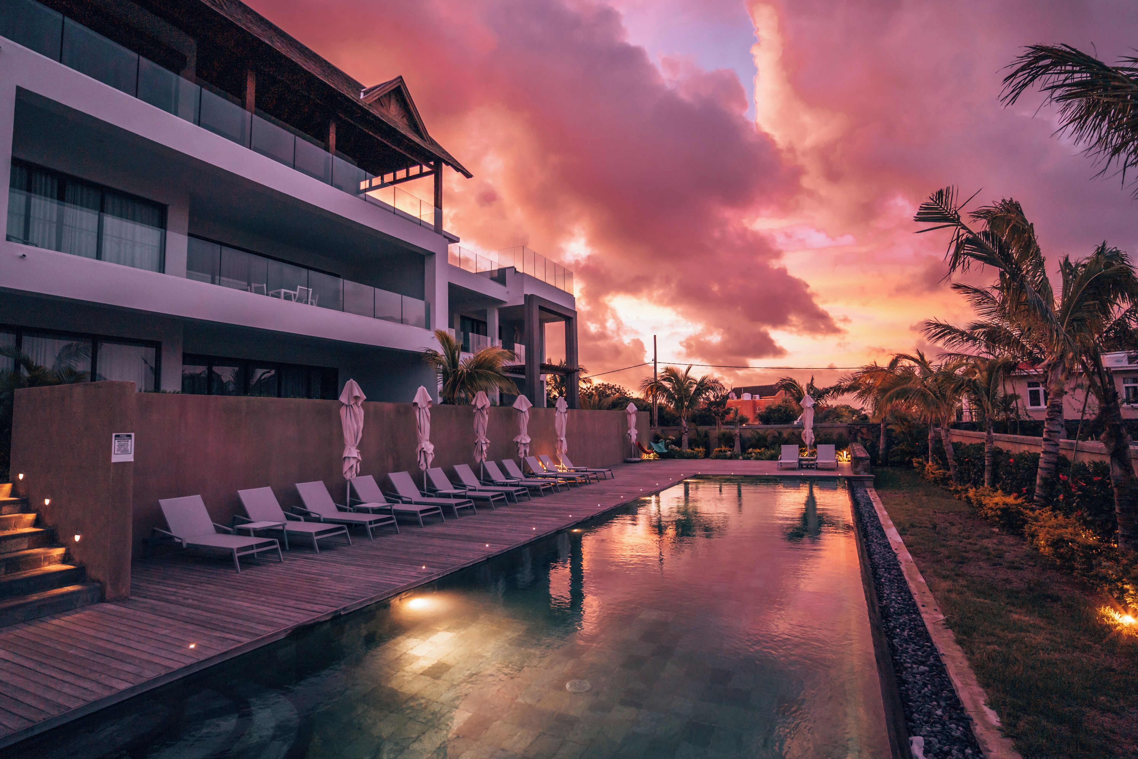 A modern hotel with a pool, lounge chairs, and a sunset view.