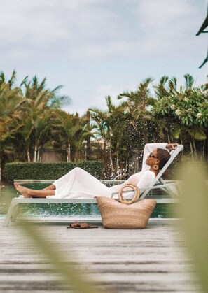A person relaxing in a poolside chair with a wicker basket beside them, surrounded by lush greenery. - Mythic Suites & Villas by MJ Holidays (Grand Gaube)