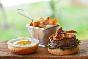 A burger with bacon, tomato, and lettuce on a bun, a fried egg, and a basket of fries. - Mythic Suites & Villas by MJ Holidays (Grand Gaube)