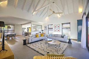 A spacious living room with a high ceiling, a large sofa set, a coffee table, and a TV.