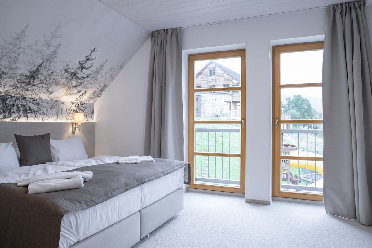 Een slaapkamer met een groot bed, een raam met uitzicht op een huis en een plafond met bladmotief.