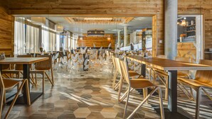 Un restaurant spacieux aux murs et au sol en bois, doté d’un mobilier moderne et d’un espace de restauration central avec une longue table et des chaises.