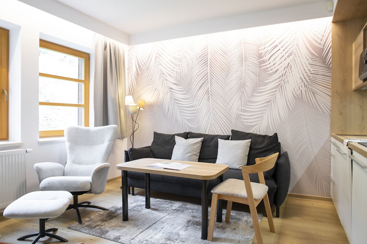 Een moderne woonkamer met een bank, fauteuil en voetenbankje, een houten tafel en een behang met patroon.