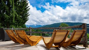 Une terrasse en bois avec des chaises longues donnant sur un paysage montagneux.