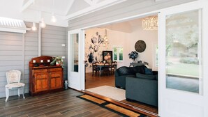 A spacious living room with a grey sofa, wooden cabinet, and a dining area with a table and chairs. - One Bedroom Cottage with a Shared Pool (Dural)