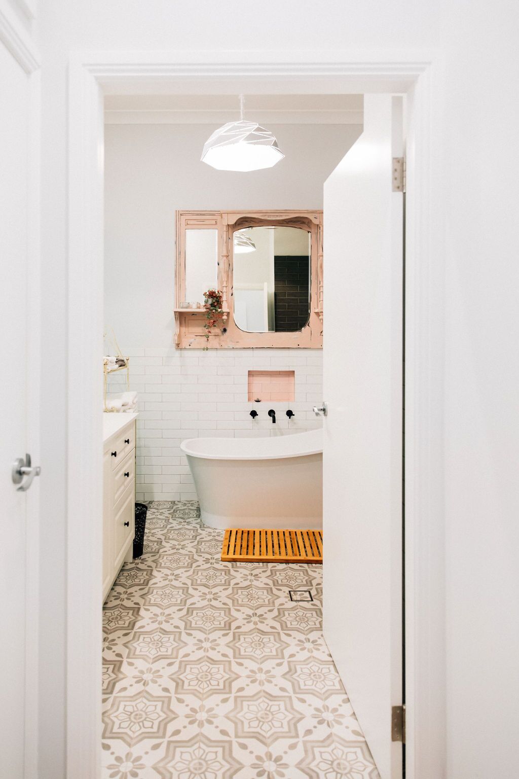 Un bagno stretto con un lavandino bianco, uno specchio e un pavimento decorato.