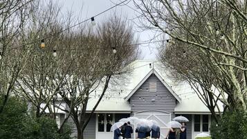 A building with a grey roof and white trim, surrounded by trees and a neatly trimmed hedge.