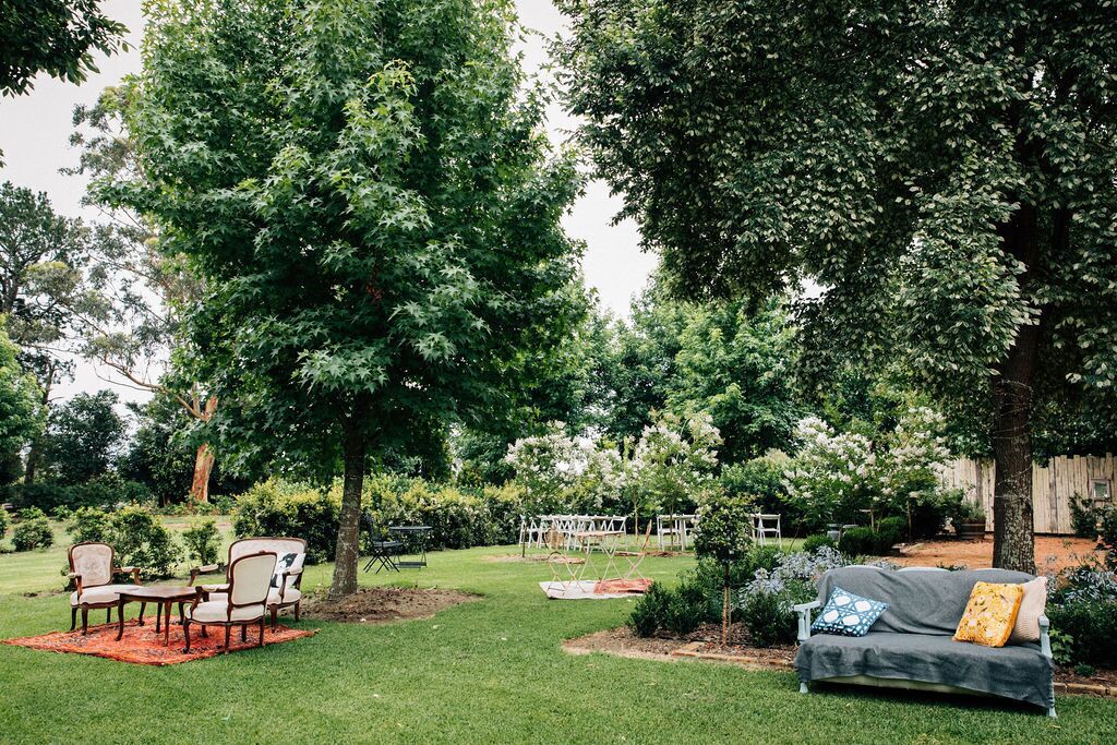 Un jardín bien cuidado con una zona de estar que incluye un sofá y sillas, rodeado de abundante vegetación y árboles.