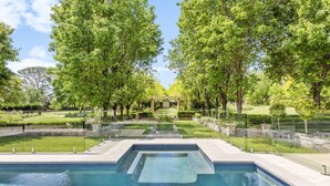 A rectangular pool with a clear blue water surface, surrounded by a paved deck and bordered by a low stone wall. - One Bedroom Cottage with a Shared Pool (Dural)