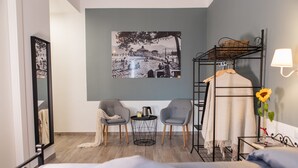A hotel room with a bed, two chairs, a small round table with a kettle, a wall-mounted lamp, a bunk bed with a hanging chair, and a framed picture on the wall. - Maeli Rooms (La Spezia)