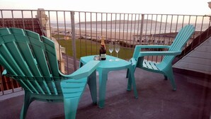 A balcony with two turquoise chairs and a small table, overlooking a beach and distant hills. - The Sunfold (Weston-super-Mare)
