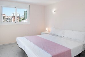 A hotel room with a bed, a nightstand, a window, and a view of buildings outside. - 107283 - Apartment in Fuengirola (Fuengirola)