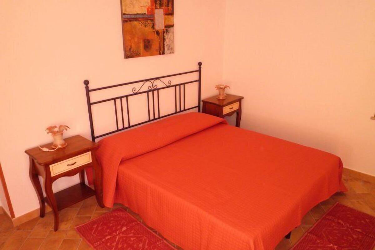 Una camera da letto con un letto, due comodini, un tavolino, un tappeto rosso e un quadro appeso al muro.