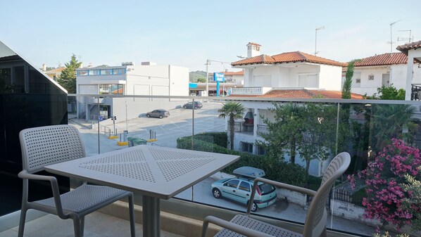 Un balcón con mesa y sillas, con vista a una calle con coches y edificios.