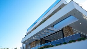 Un edificio moderno de varios pisos con techo plano, ventanas amplias y un balcón con barandilla de vidrio.