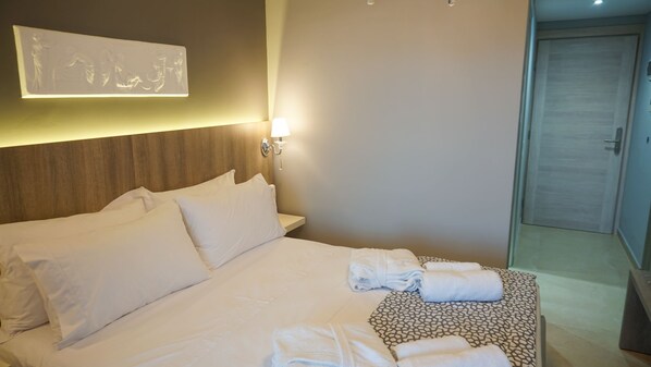 Una habitación de hotel con una cama grande, una mesita de noche con toallas, una lámpara de pared y una puerta.