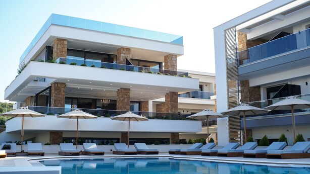 Un hotel moderno de varios pisos con piscina, sillas de tomar el sol y sombrillas exteriores.