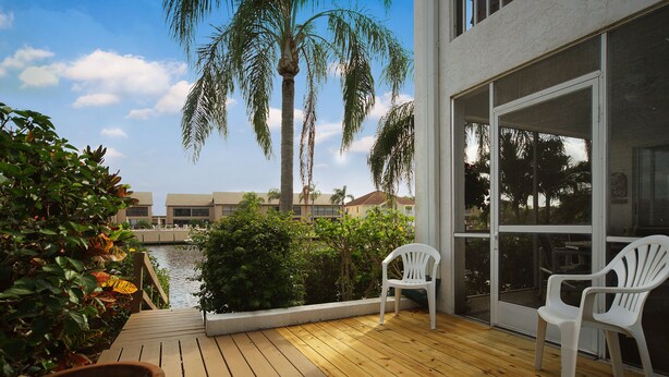 A wooden deck with two white chairs, a view of a water body, and a building with large windows.