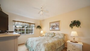 A bedroom with a bed, nightstands, a ceiling fan, a window with curtains, and a wall-mounted plant.