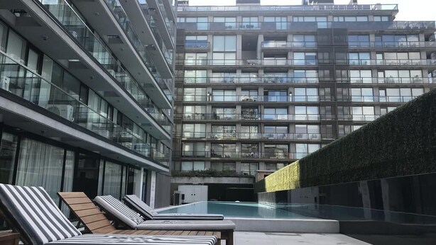 Een modern gebouw met een zwembad op het dak, inclusief ligbedden en een glazen wand.