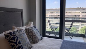 Een hotelkamer met een groot bed, gekleurde kussens en uitzicht op een balkon met buitenmeubilair.