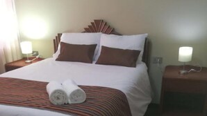 A neatly made bed with a striped bedspread, two pillows, and two rolled towels on the bed. There are two bedside tables with lamps, one on each side of the bed. - Mística Boutique Hotel (Arequipa)