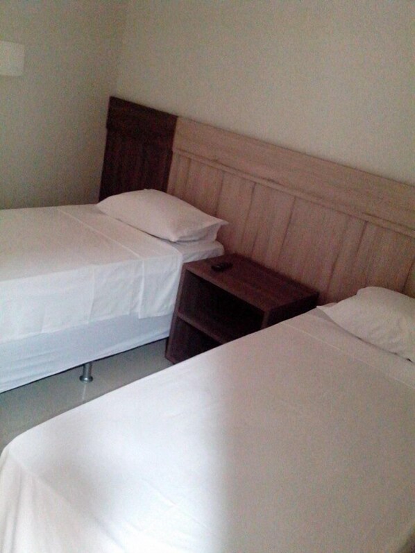 Una habitación sencilla con dos camas, cada una con ropa de cama blanca y cabeceros de madera.