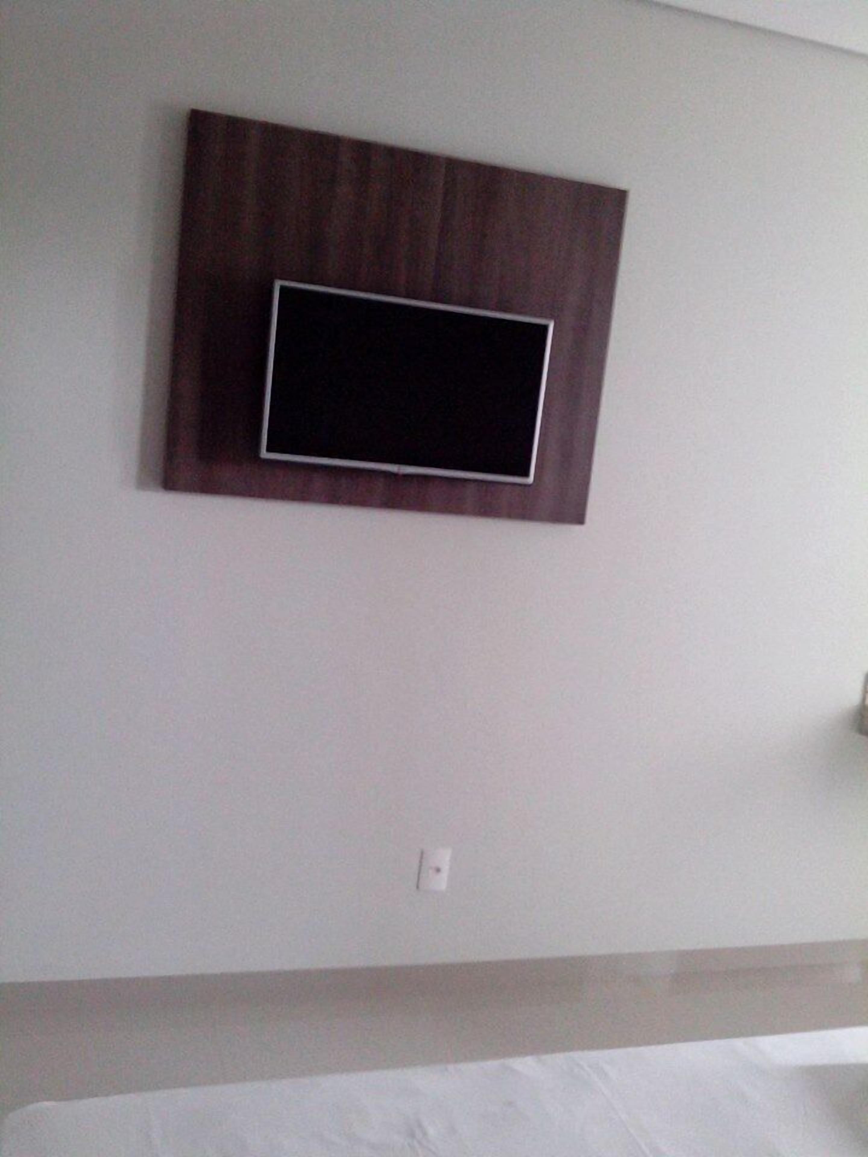 Una habitación con cama, televisión montada en la pared y un interruptor de luz.
