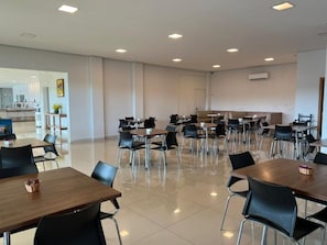 A spacious dining area with multiple tables and chairs, a kitchen in the background, and a clean, modern design. - Hotel PetroShop (Palmas)