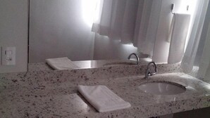 Casa de banho com bancada de granito, pia, espelho e toalha.
